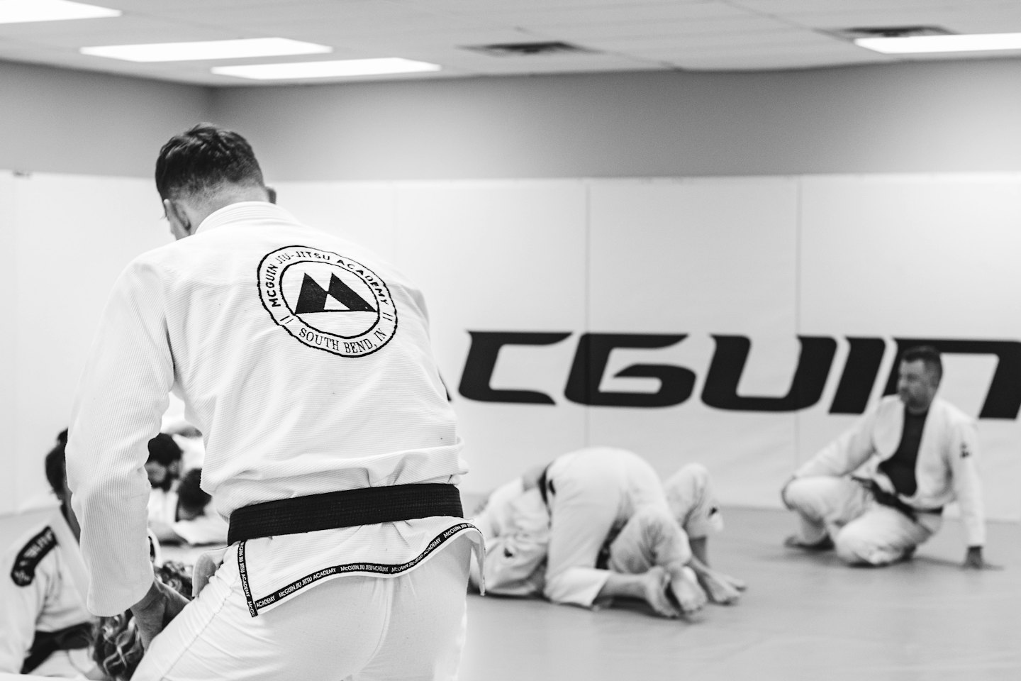People practice Brazilian Jiu-Jitsu on mats in a gym.