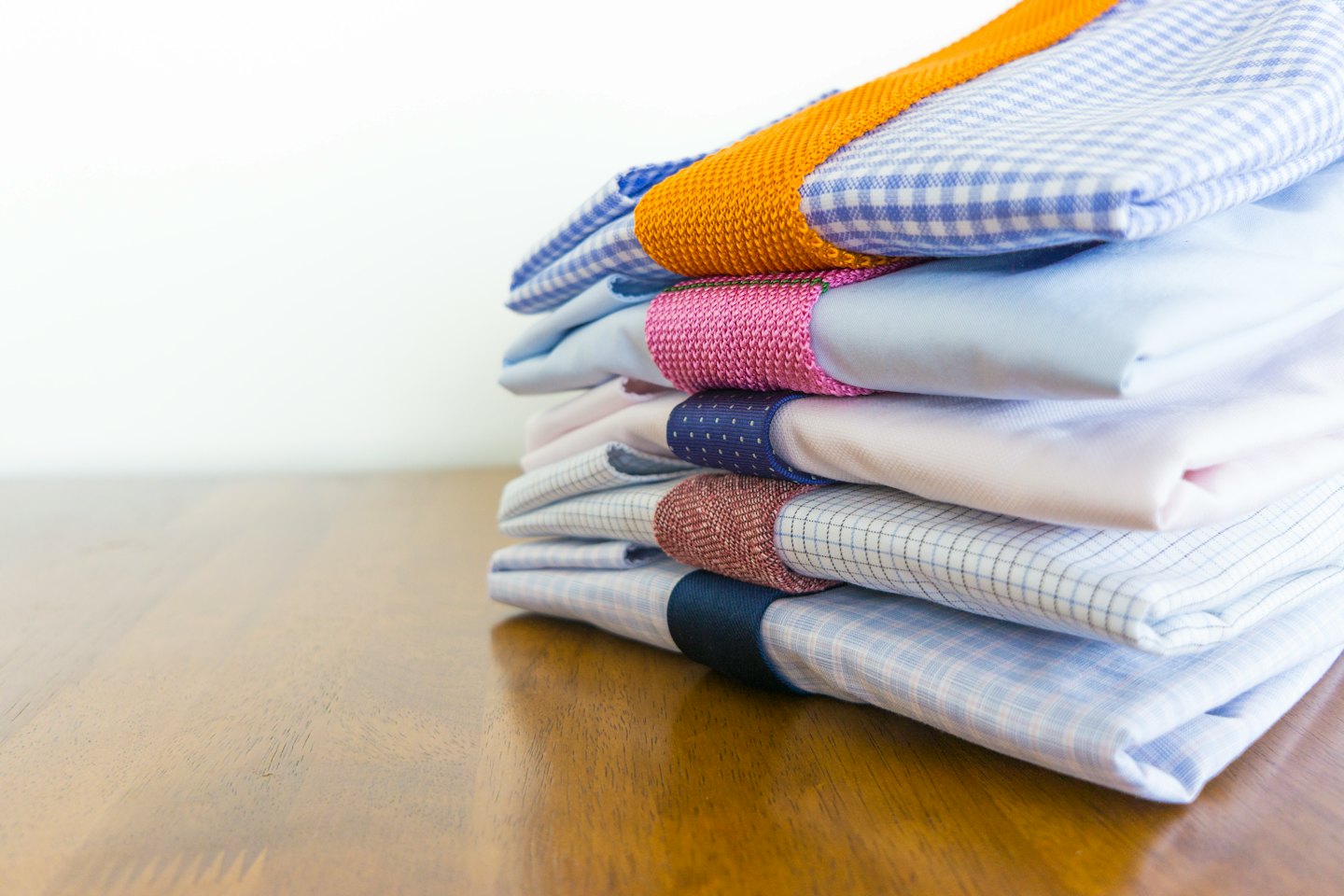 Five neatly folded dress shirts stacked on a wooden surface.
