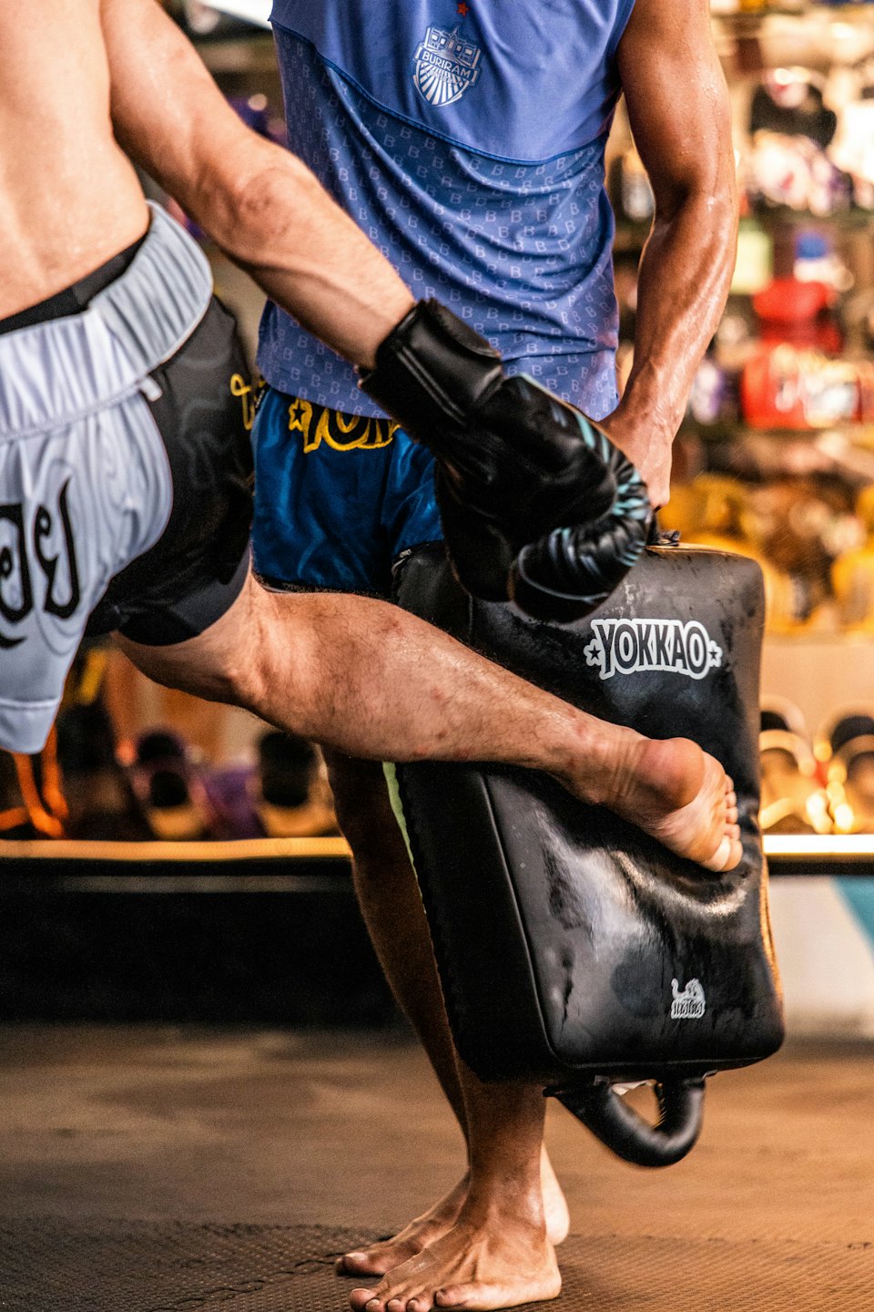 Two people practicing martial arts kicks in a gym.