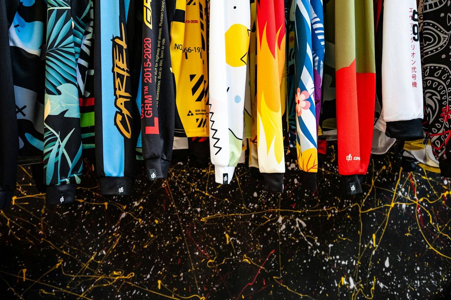 Colorful patterned shirts hang against a paint splattered wall.
